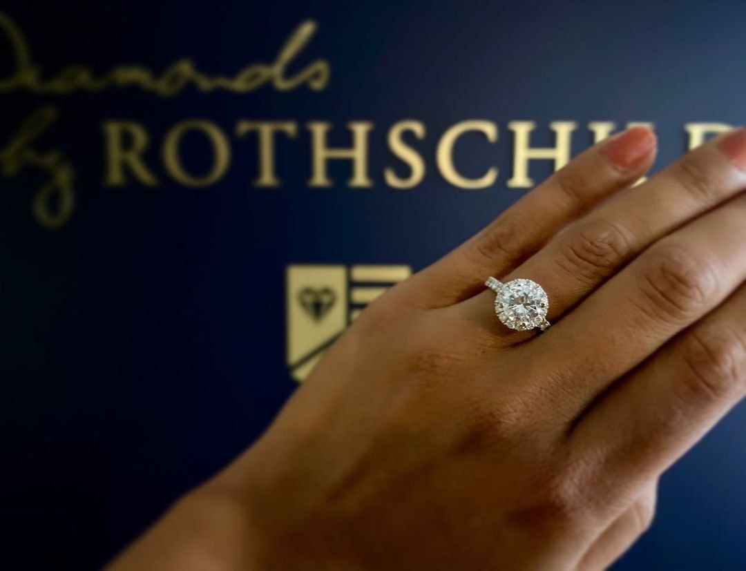 Hand with halo engagement ring in front of the Diamonds by Rothschild signage