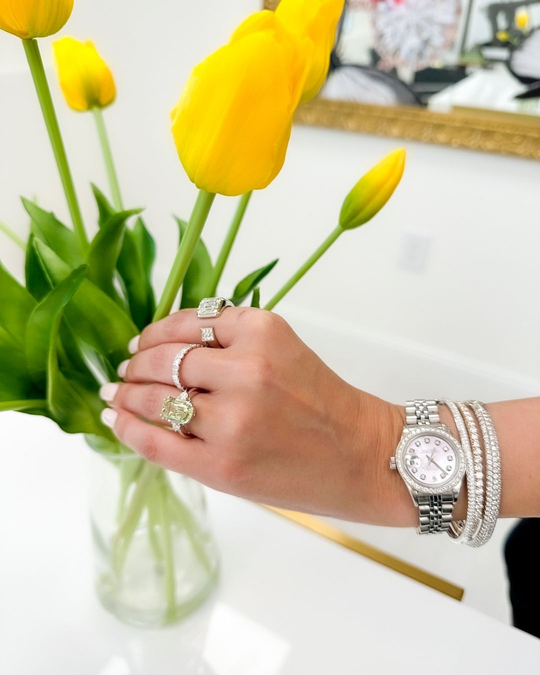Lady hand with diamond rings, watch and bracelets holding a yellow flower
