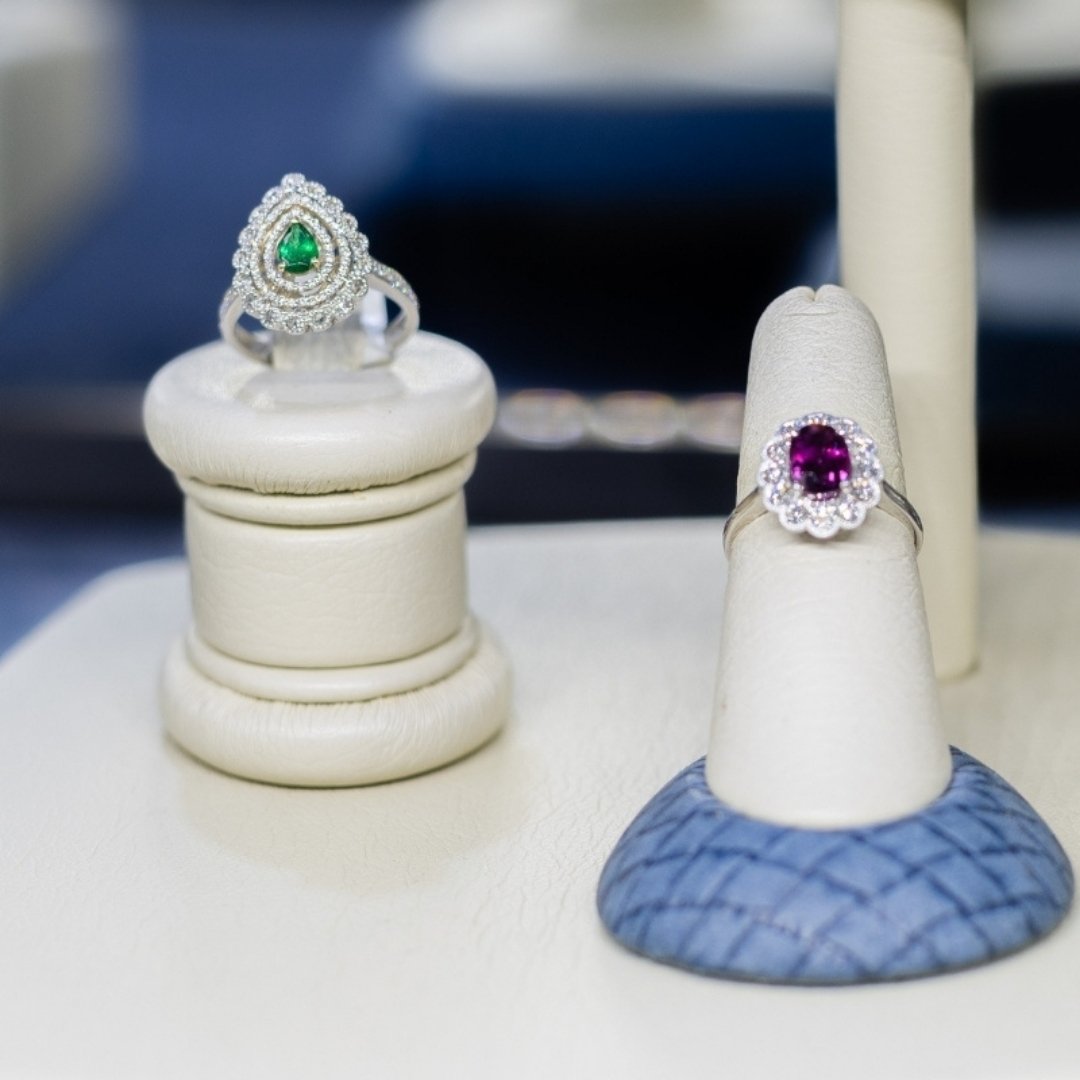 Two rings with colored center gemstones on decorative stands with a blurred background