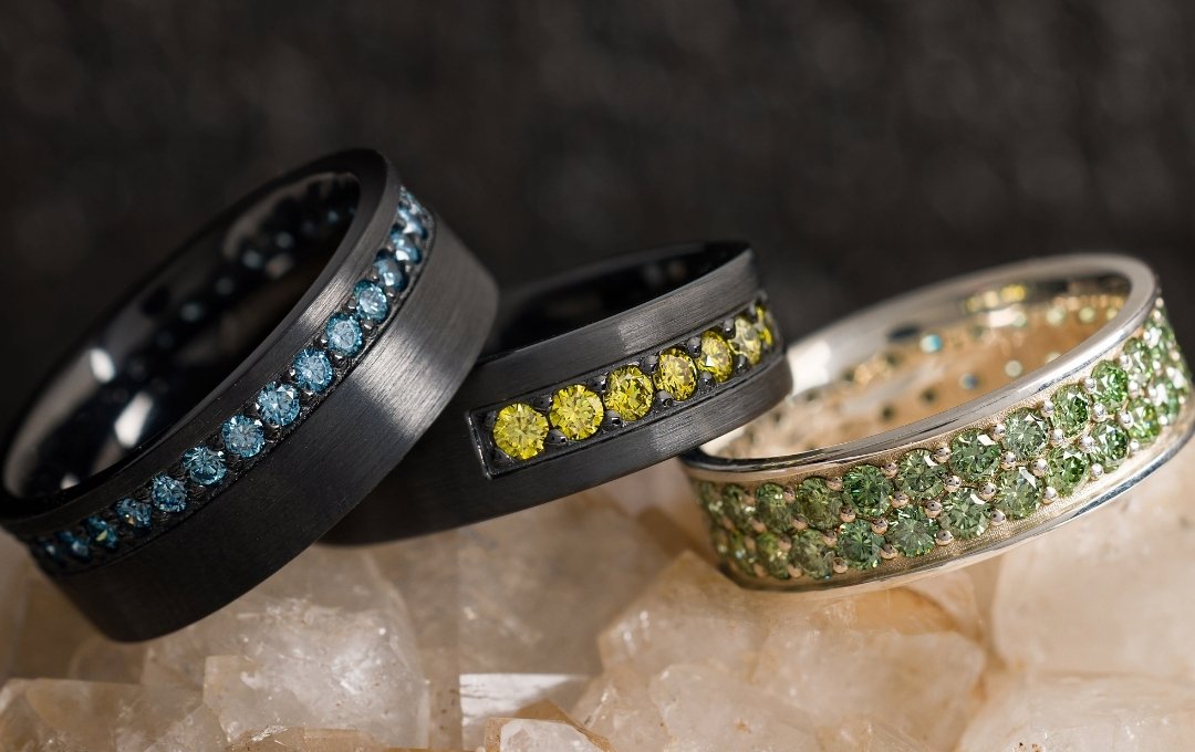 Three Lashbrook rings with colored gemstones on a textured surface