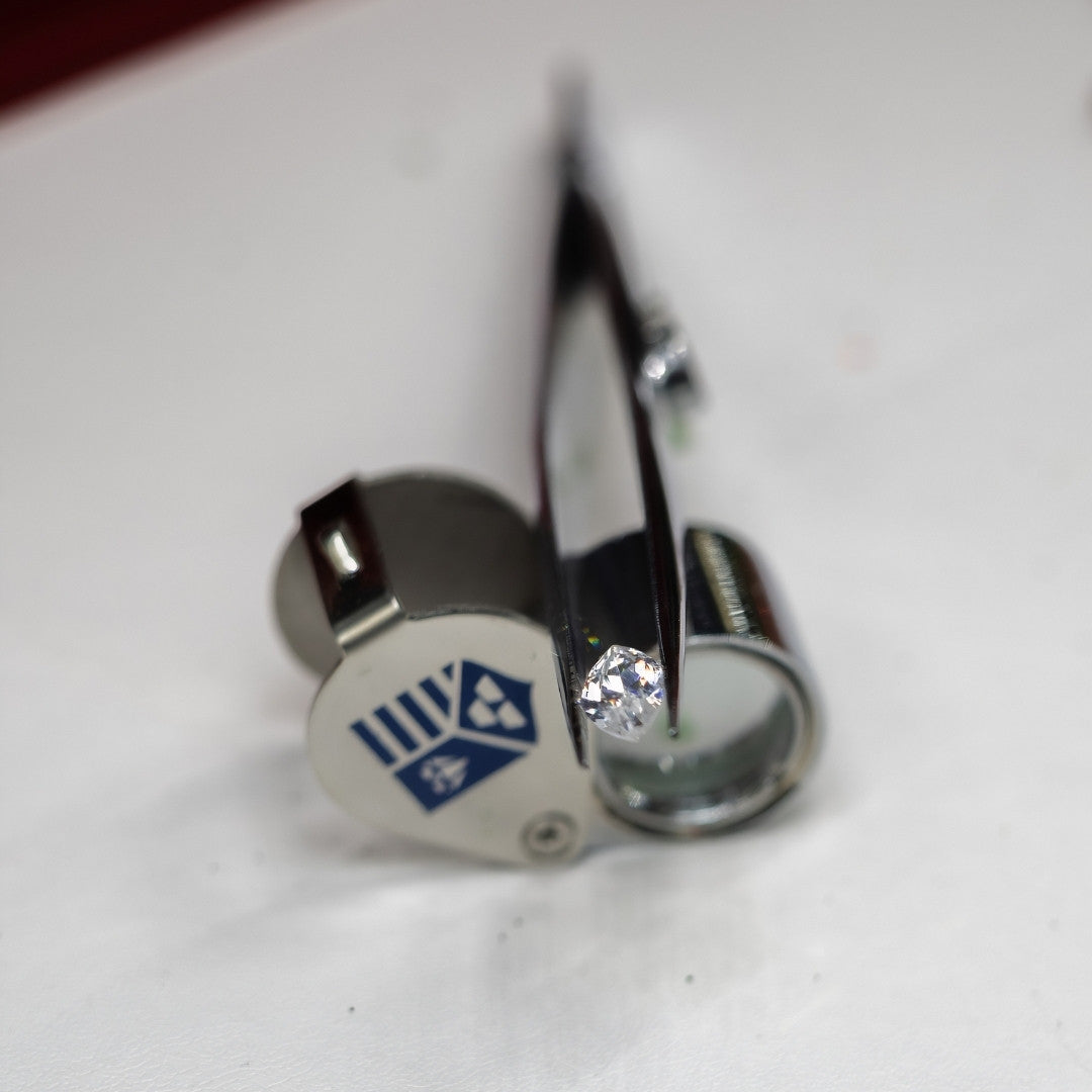 Close-up of a diamond in a gemological tweezer on top of a loupe with a visible brand logo.