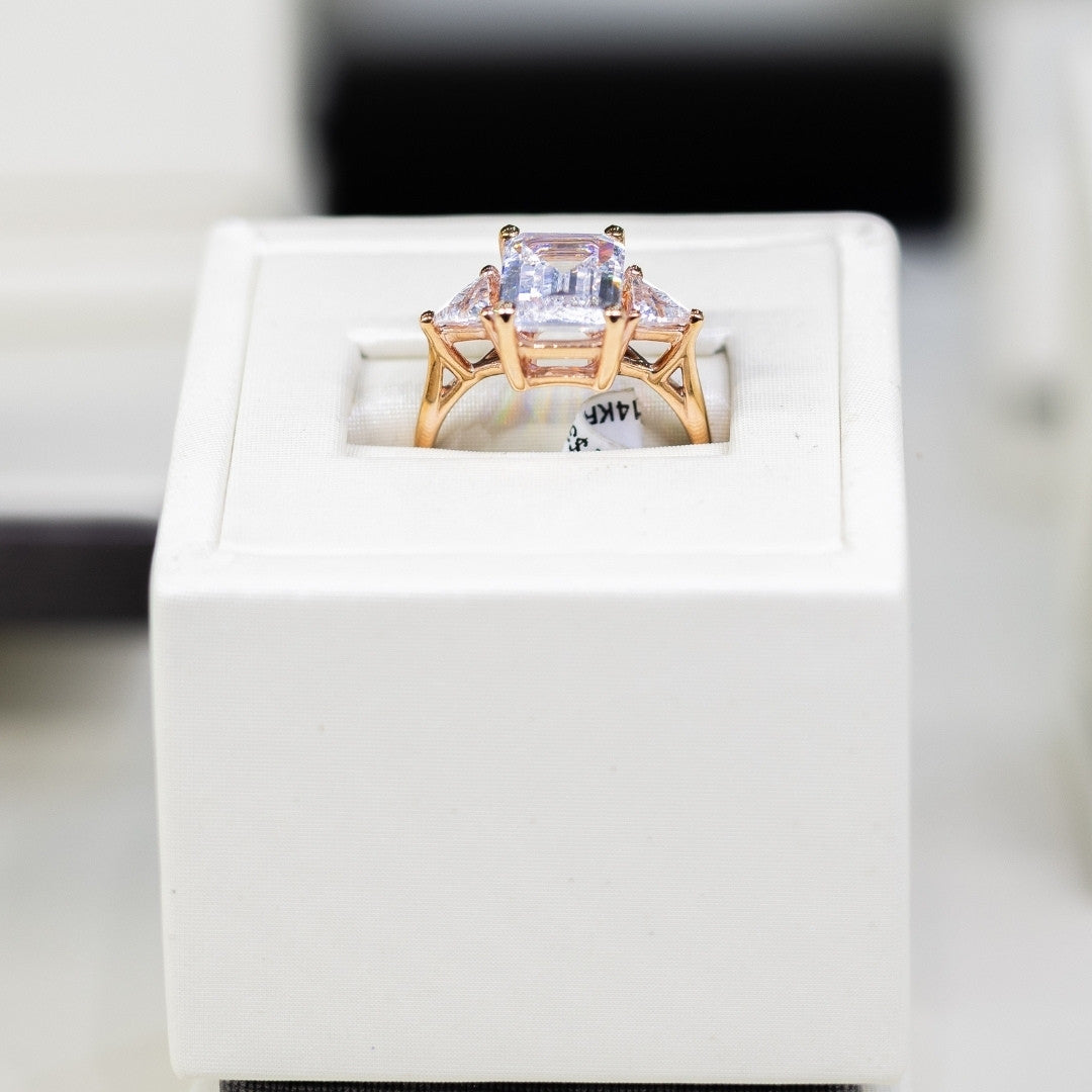 Yellow gold ring with a large emerald cut diamond and two side stones on a white cushion